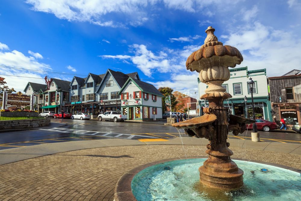 Charming coastal town scene with fountain, colorful buildings, and blue sky in Bar Harbor, Maine.