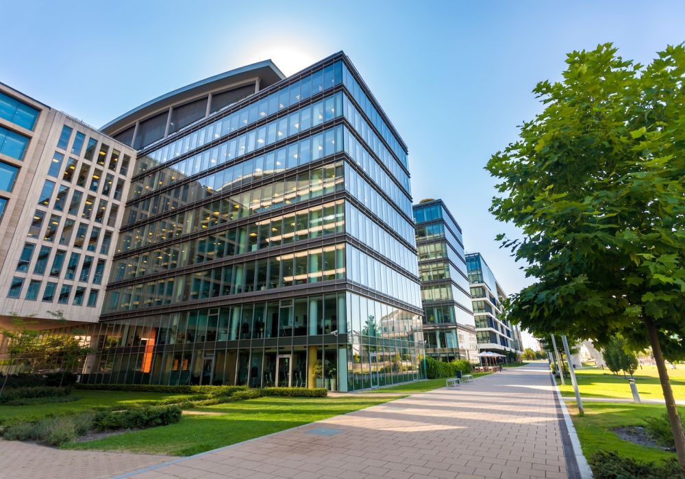 Modern office buildings with glass facades and a green walkway under a clear blue sky.