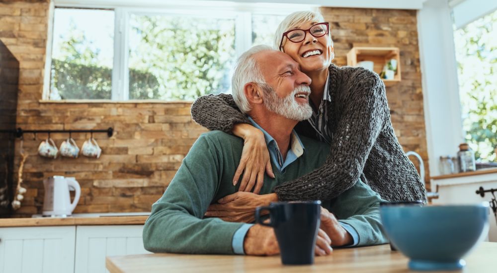 Happy senior couple embracing in cozy kitchen, enjoying morning coffee together.