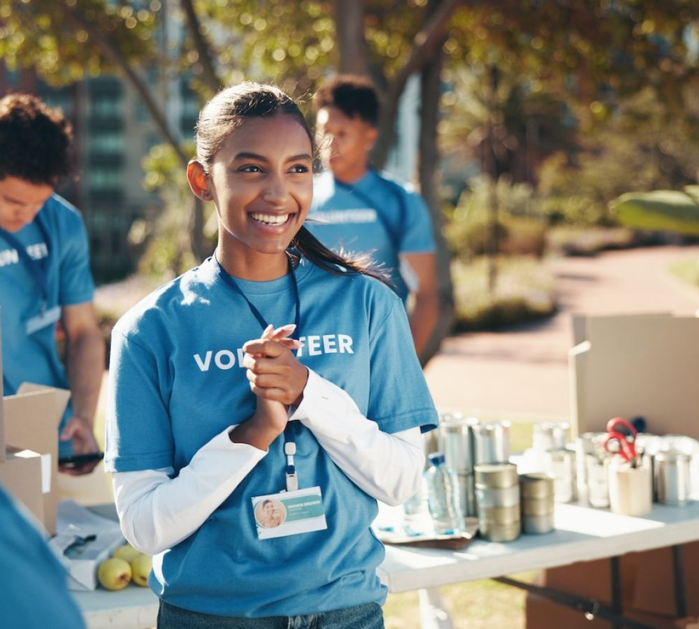 Smiling volunteers sorting donations at an outdoor event, wearing blue shirts and name badges.