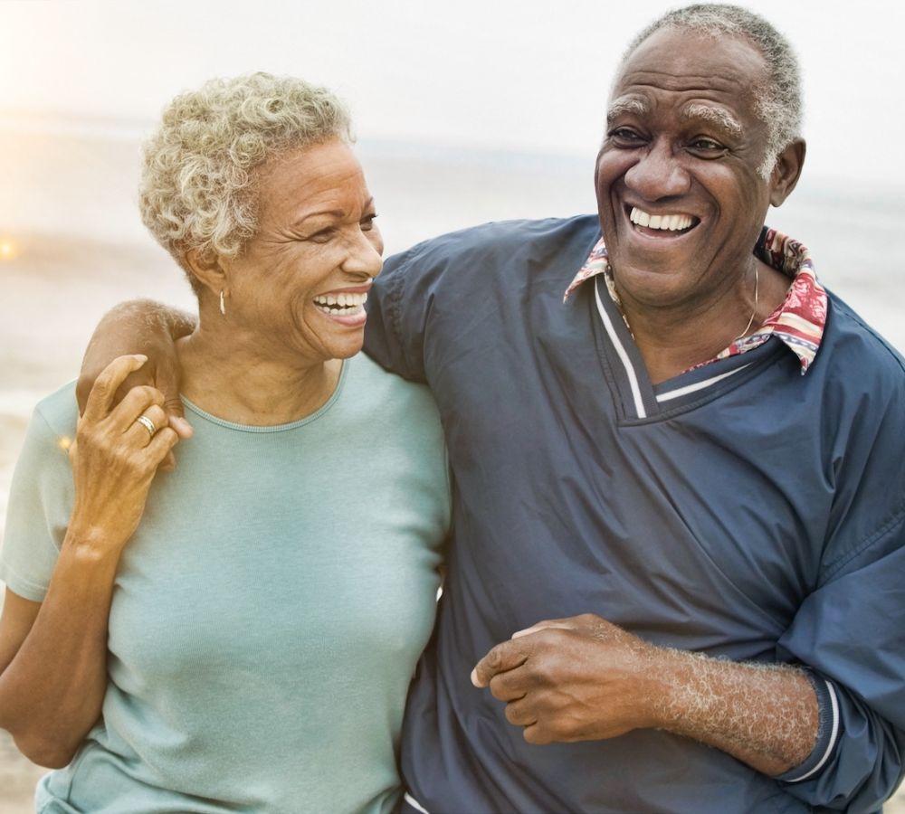 Happy older couple laughing together on a beach, enjoying a sunny day by the sea.