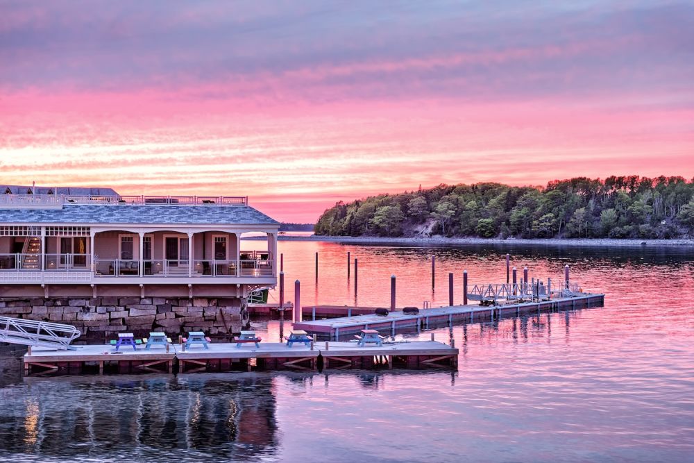 Sunset over waterfront lodge and dock, reflecting vibrant pink and orange hues on a tranquil lake.