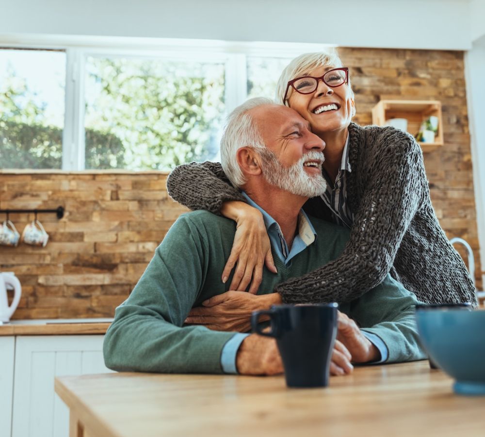 Happy senior couple embracing in cozy kitchen, enjoying morning coffee together.