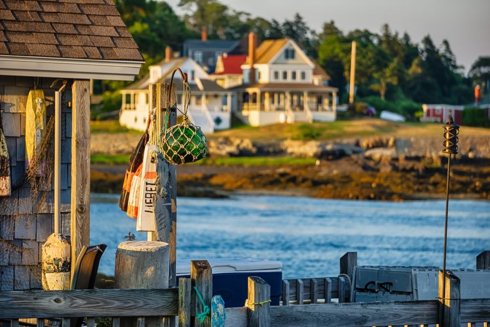 Coastal scene with fishing gear hanging on a dock, with houses and trees in the sunny background.