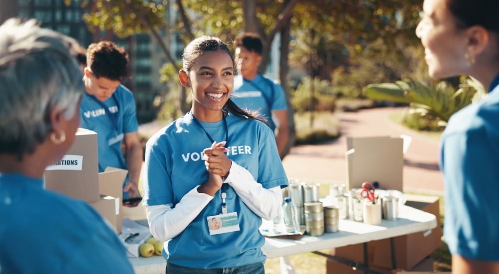 Smiling volunteers sorting donations at an outdoor event, wearing blue shirts and name badges.