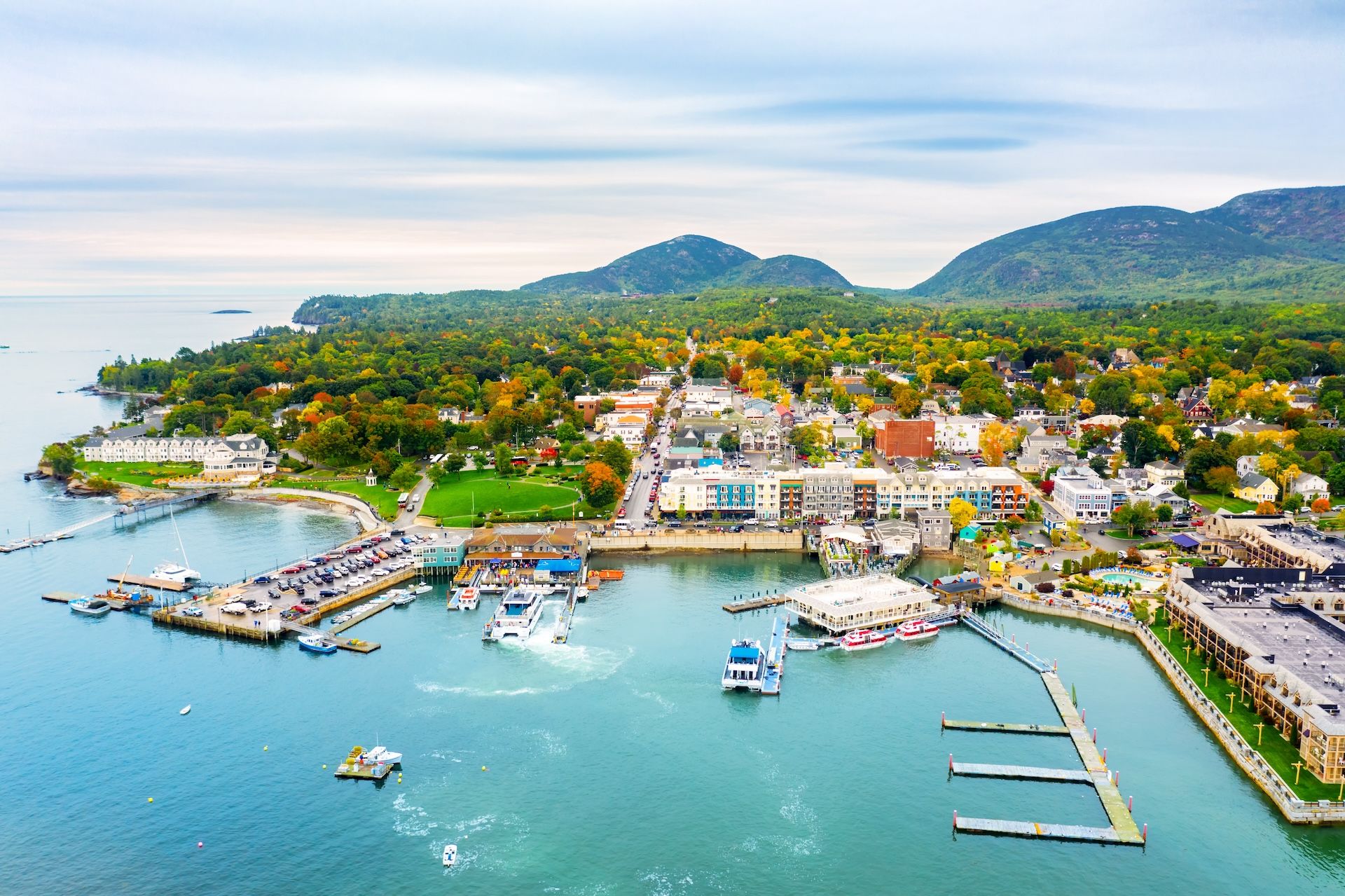 Aerial view of a coastal town with docks, colorful buildings, lush greenery, and mountains in the background.