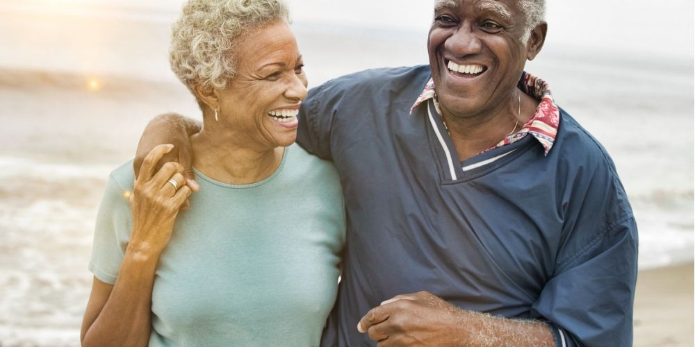 Happy older couple laughing together on a beach, enjoying a sunny day by the sea.
