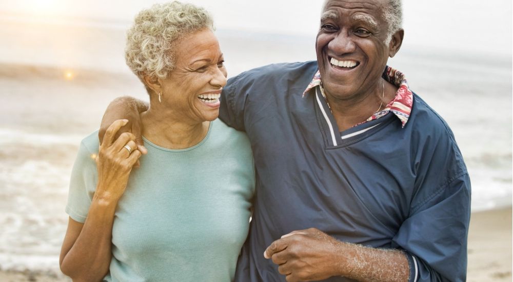 Happy older couple laughing together on a beach, enjoying a sunny day by the sea.