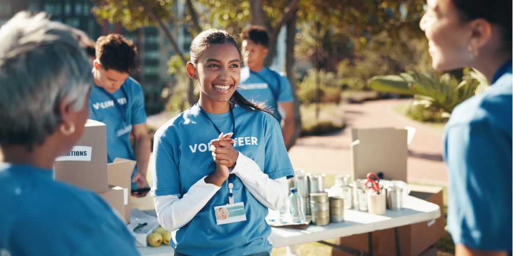 Smiling volunteers sorting donations at an outdoor event, wearing blue shirts and name badges.